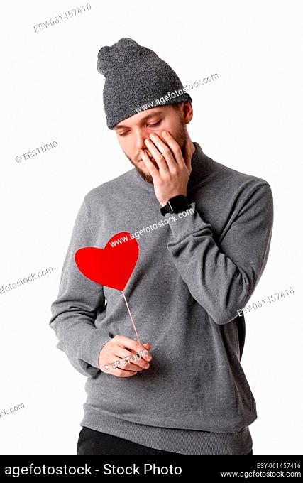 sad man in gray hat holding red paper heart isolated on white background