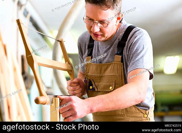 Carpenter working on a hand saw cutting a tenon in drawers in his workshop with bow or frame saw