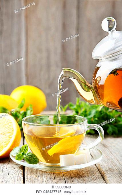Pouring tea into cup of tea on grey wooden background