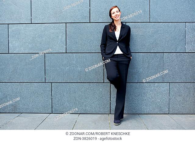 Lässige lächelnde Geschäftsfrau in der Stadt lehnt an einer Wand
