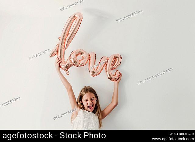 Cheerful girl with love balloon in front of wall