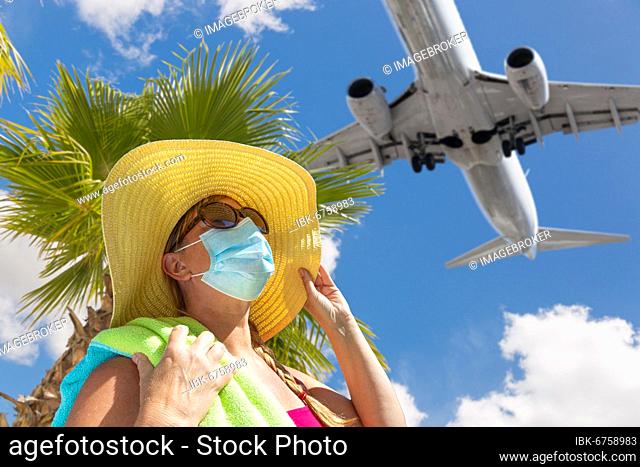 Girl with towel, hat, sunglasses and face mask under palm tree and airplane