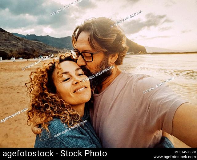 Happy adult couple in love enjoy leisure summer holiday vacation together taking selfie picture with mobile phone. Man kissing woman smiling