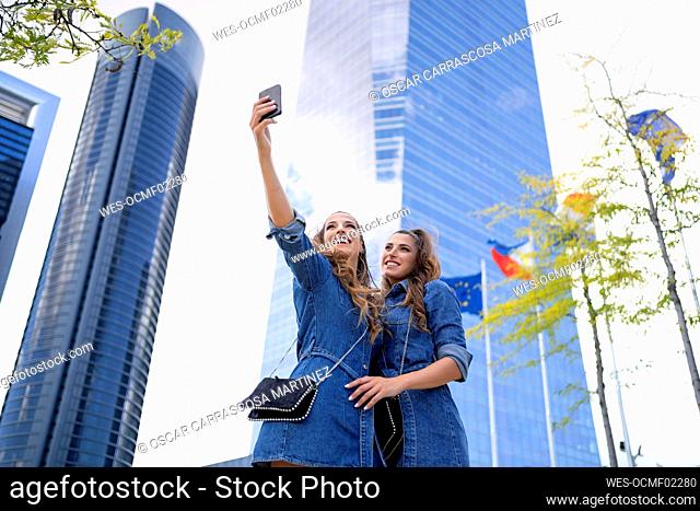 Happy women taking selfie through mobile phone in city
