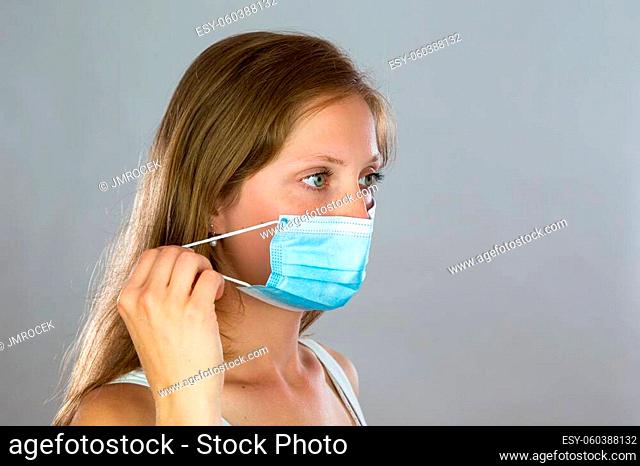 Close-up of a young woman removing face mask from head with her fingers. Caucasian blonde taking off surgical protection during coronavirus pandemic