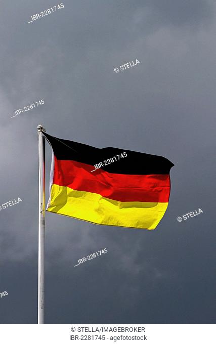 The German national flag, dark clouds at the back, symbolic image