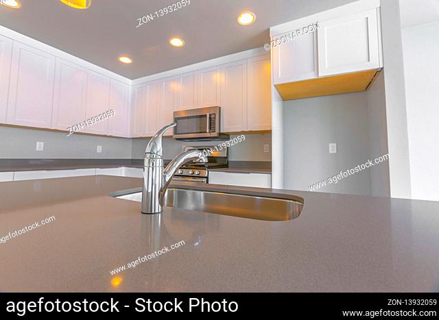 Modern kitchen of a new home with close up on the shiny faucet and sink. Cabinets, refrigerator alcove, cooking range and microwave can also be seen inside this...