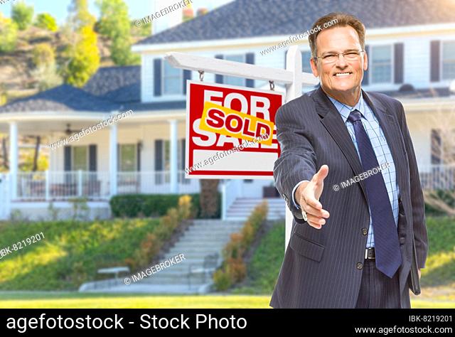 Smiling male agent reaching for a hand shake in front of beautiful house and sold real estate sign