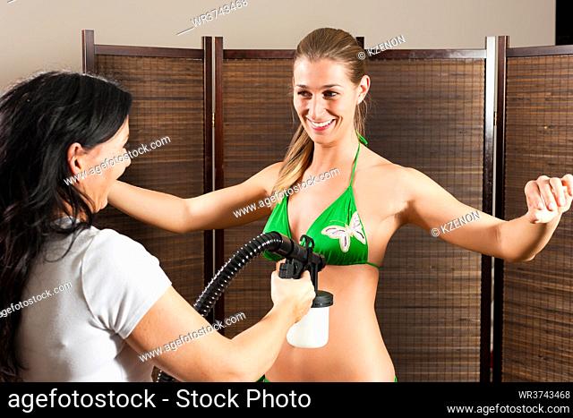 Beautician with airbrush-pistol and client in a cosmetic studio doing bronzing