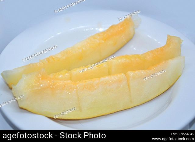 Fresh yellow melon is on a plate and cut into a wedges