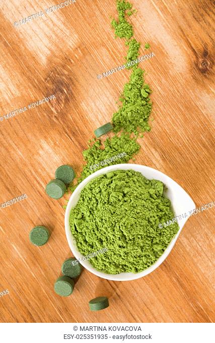 Detox. Chlorella pills and wheat grass powder in bowl on brown wooden background. Natural alternative medicine, weight loss and detox