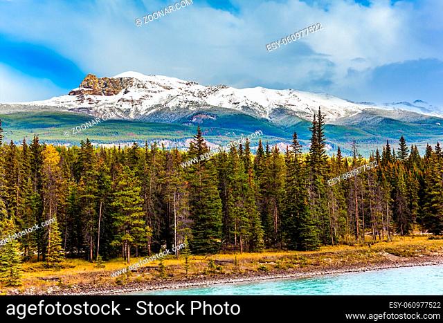 Scenic autumn in the Rockies of Canada. The lake among the snow covered mountains and coniferous forests. Thunderclouds swirl in the sky