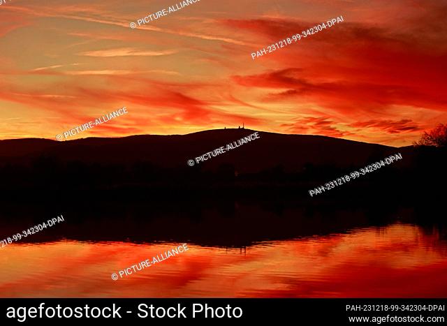 18 December 2023, Saxony-Anhalt, Wernigerode: In the light of the setting sun, the Harz mountains with the Brocken are reflected in a pond near Wernigerode