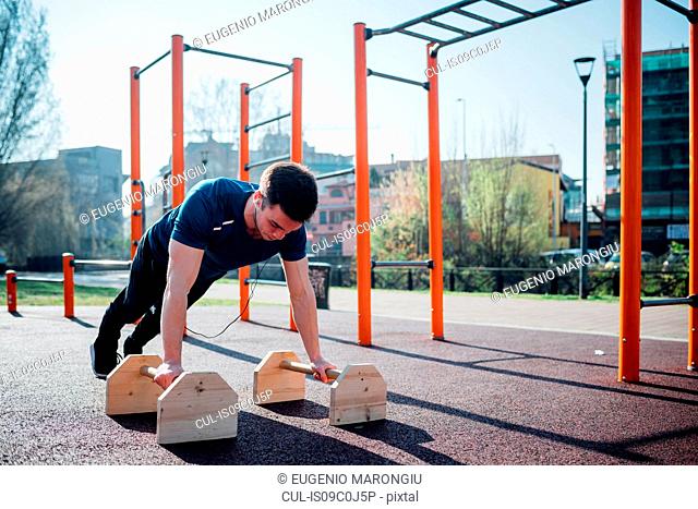 Calisthenics at outdoor gym, young man doing push ups on exercise equipment