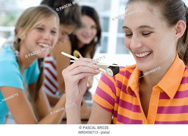 Close-up of a young woman eating with chopsticks with her friends sitting in the background