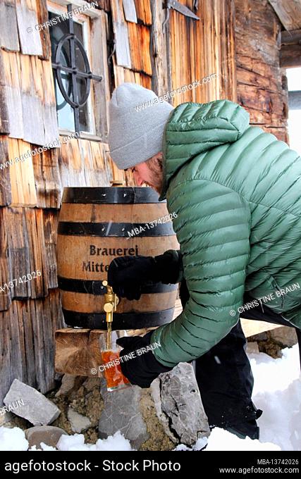 Young man pouring beer, beer barrel, Mittenwald brewery, mountain hut, winter, atmospheric