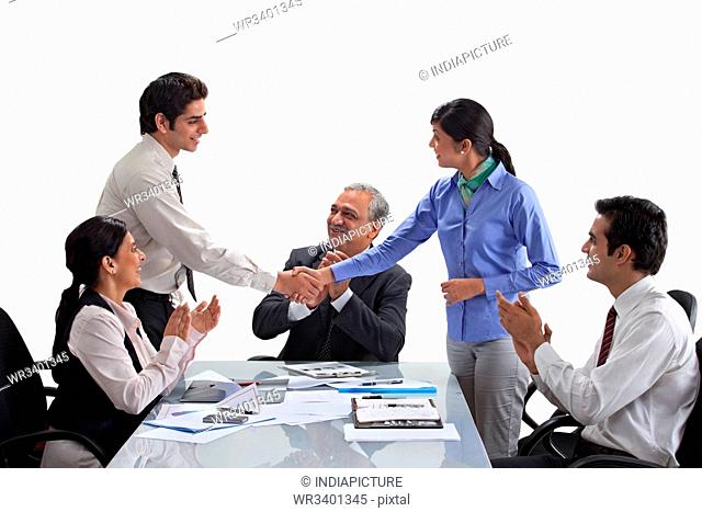 Executives shaking hands with businesspeople applauding