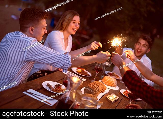 group of friends toasting red wine while having picnic or french dinner party on summer holiday vacation near the river at night