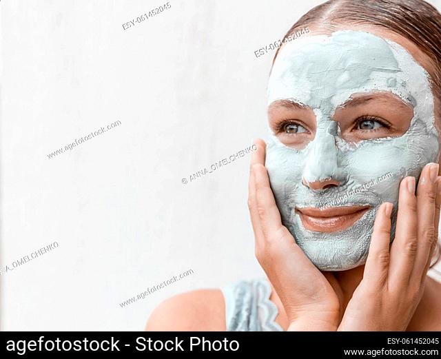 Portrait of a Beautiful Young Woman Applying Clay Mask Isolated on White Background. Enjoying Day Spa in Beauty Clinic