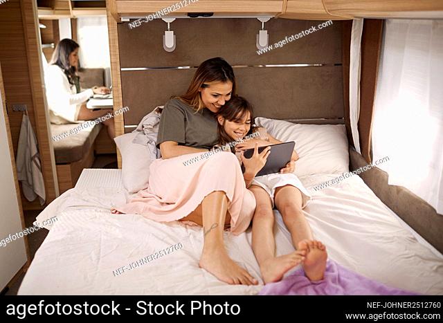 Mother and daughter sitting on bed in camper van