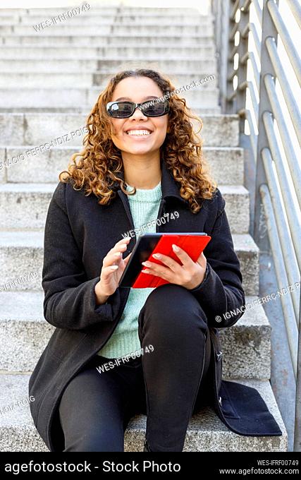 Smiling young woman with digital tablet sitting on staircase