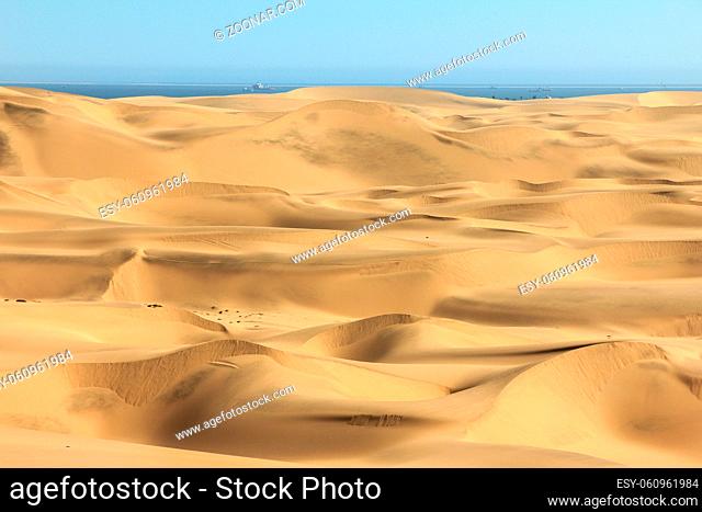 Sand dune desert meets water of the Atlantic Ozean. Ships and boats on the water