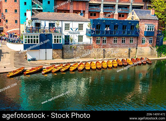 Durham, United Kingdom - April 30, 2019: Line of moored rowing boats on the banks of River Wear near a boat club in Durham