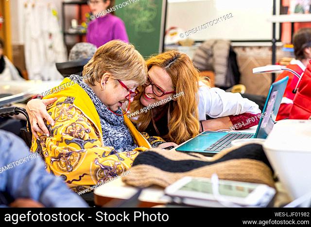 Smiling female caregiver talking with disabled woman by laptop at rehabilitation center