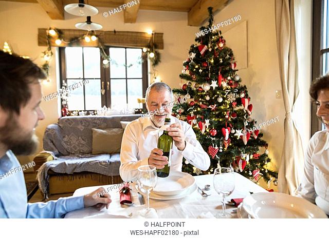 Smiling senior man with family holding bottle of wine at Christmas dinner table