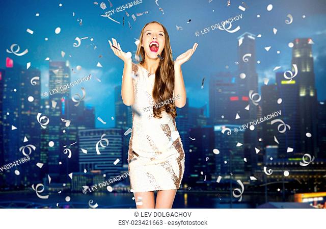 people, holidays, emotion and glamour concept - happy young woman or teen girl in fancy dress with sequins and confetti at party over night singapore city...