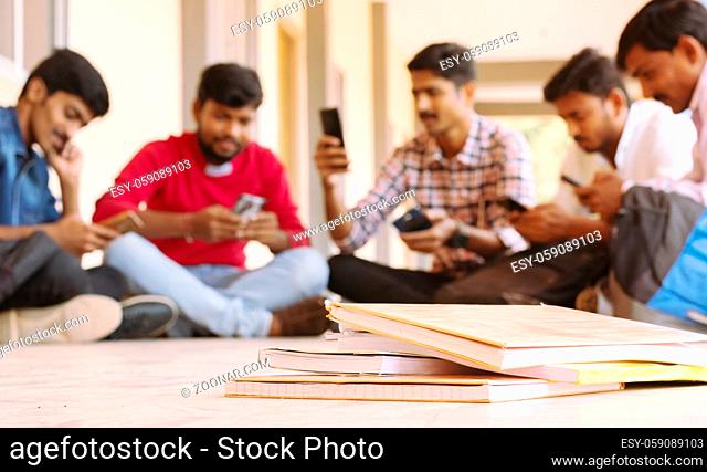 selective focus of Books, Group of students busy on mobile by avoiding books during exams at college - Teenager students on smartphone video game addiction...