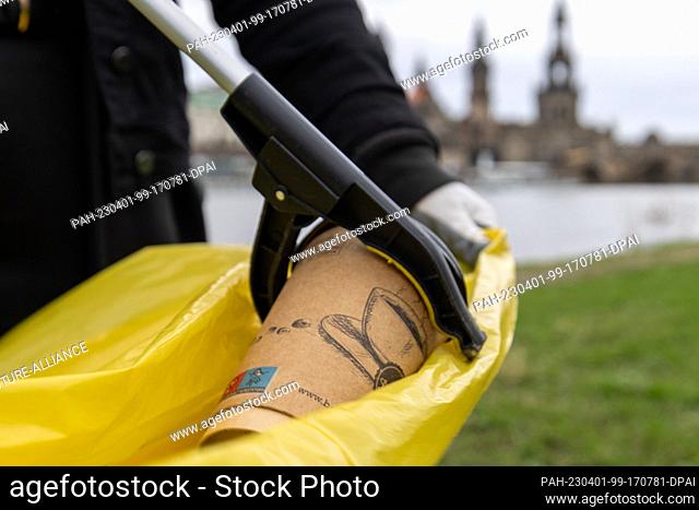 01 April 2023, Saxony, Dresden: A coffee cup is put into a yellow bag with a grabber during the Elbe Meadows Cleaning Action Day in the city of Dresden
