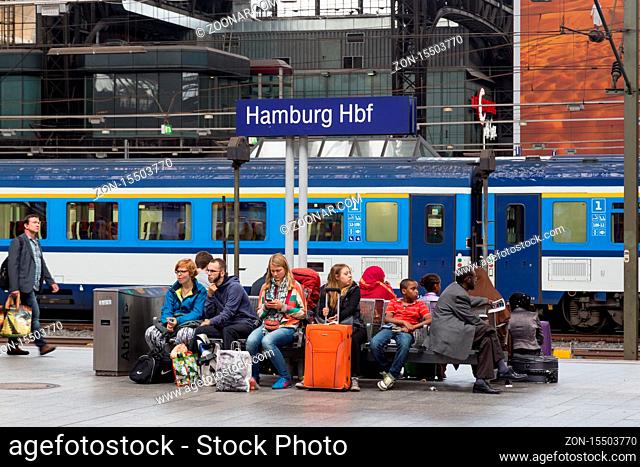 Hamburg, Germany - August 5, 2016: Group of people sitting under a signpost on the platform of the central station waiting for their train