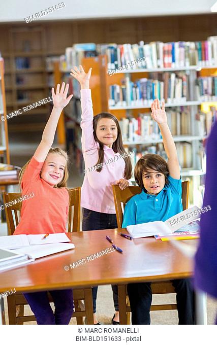 Students raising their hands in library