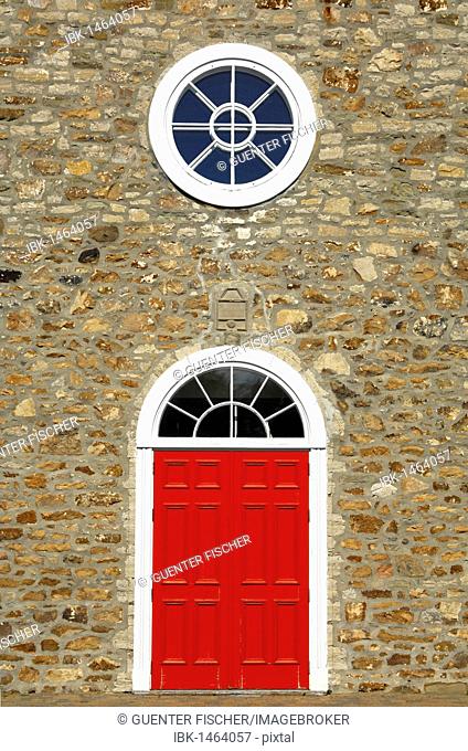 Red door and white round window of the Saint-Pierre-et-Saint-Paul Church, historic monument in the town of St-Pierre-de-l'Ile-d'Orleans, on Orléans Island