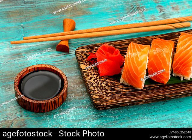 Close up one set of six Philadelphia sushi rolls with raw salmon served on palm wood plate on blue table, higgh angle view