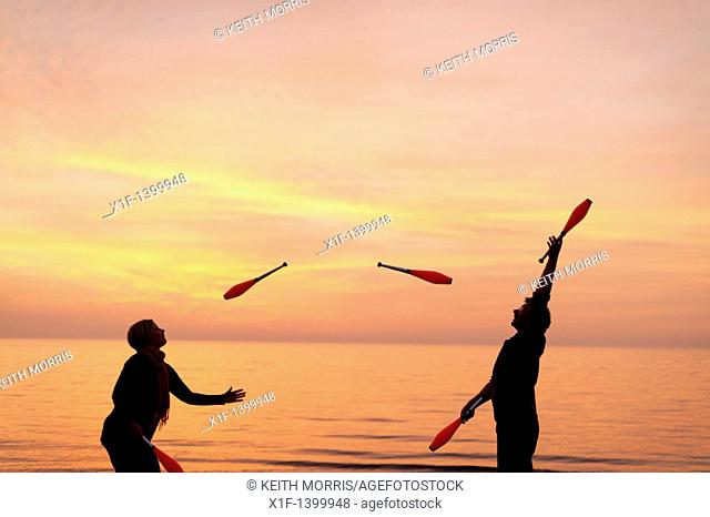 A young couple Juggling with clubs on the beach, spring evening sunset, Aberystwyth Wales UK