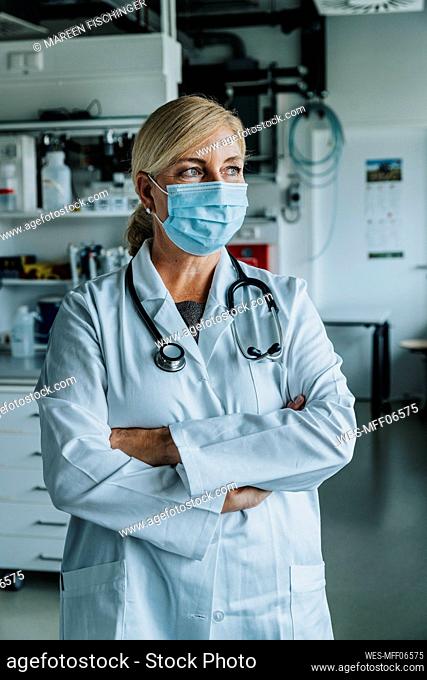 Scientist wearing face mask standing with arms crossed at laboratory