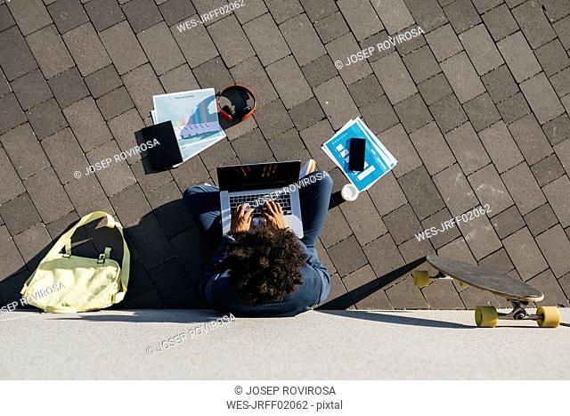 Young businessman sitting outdoors at a wall working on laptop