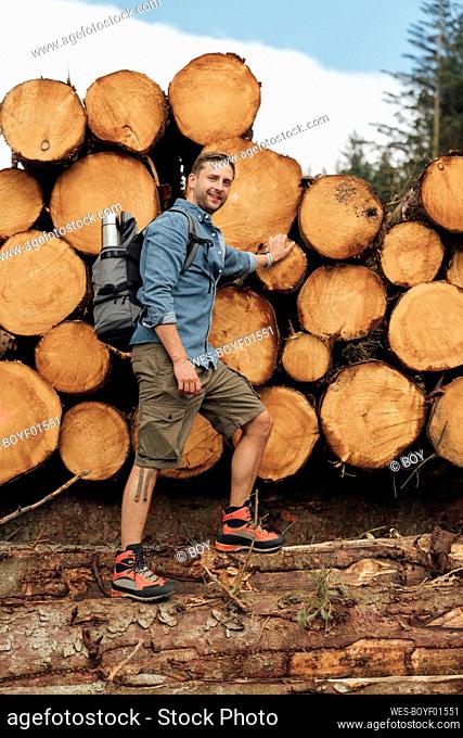 Smiling mid adult man standing on log by woodpile in forest