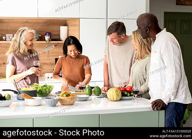 Group of diverse middle-aged friends chatting at kitchen island while cooking meal