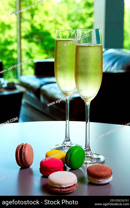 Two glasses of sparkling wine or champagne on a table with small colorful macaroons