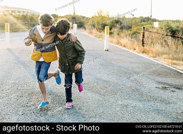 Boys helping each other to walk in one leg by entrance park at sunrise