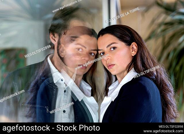 Couple separated through glass pane, woman looking at camera