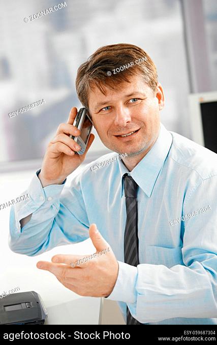 Portrait of businessman in office, talking on smartphone, gesturing