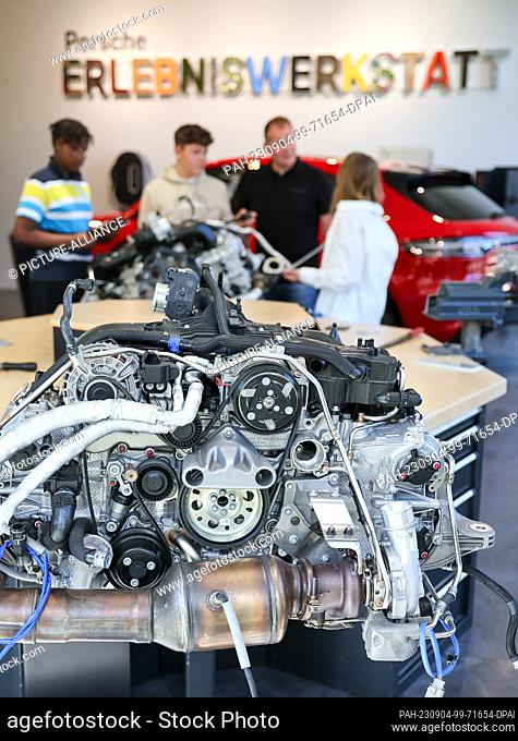 04 September 2023, Saxony, Leipzig: Instructor Lars Bergemann (2nd from right) explains a 4-cylinder boxer engine to students in the Porsche experience workshop