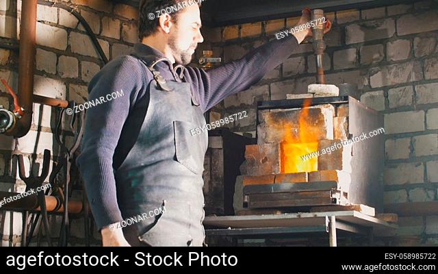 Blacksmith regulates the fire in the furnace with hot metal, close up