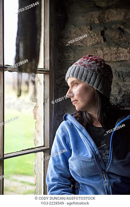 Female hiker looks out window of Burnmouth Bothy, Rackwick Bay, Hoy, Orkney, Scotland