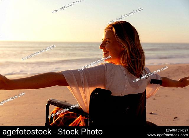Smiling woman on wheelchair with her arms wide open at the beach