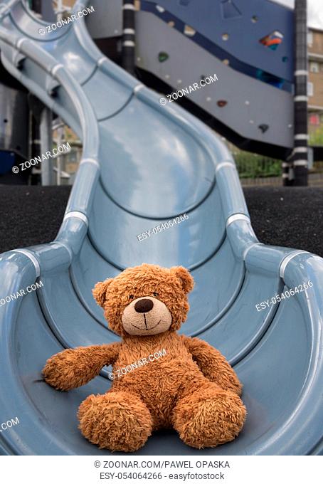 Cute little brown teddy bear at the bottom of big outdoor slide in the playground area